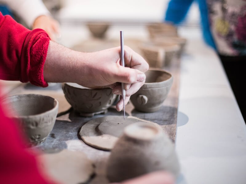 A person using pottery tools to decorate their handmade pottery bowl